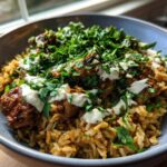 Close-up of a bowl of One Pot Chicken Shawarma Rice topped with seasoned chicken, white sauce, and fresh parsley.