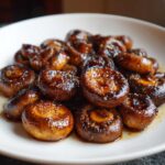 A close-up of glossy, caramelized Oven-Roasted Mushrooms with Soy Sauce and Honey piled on a white plate.