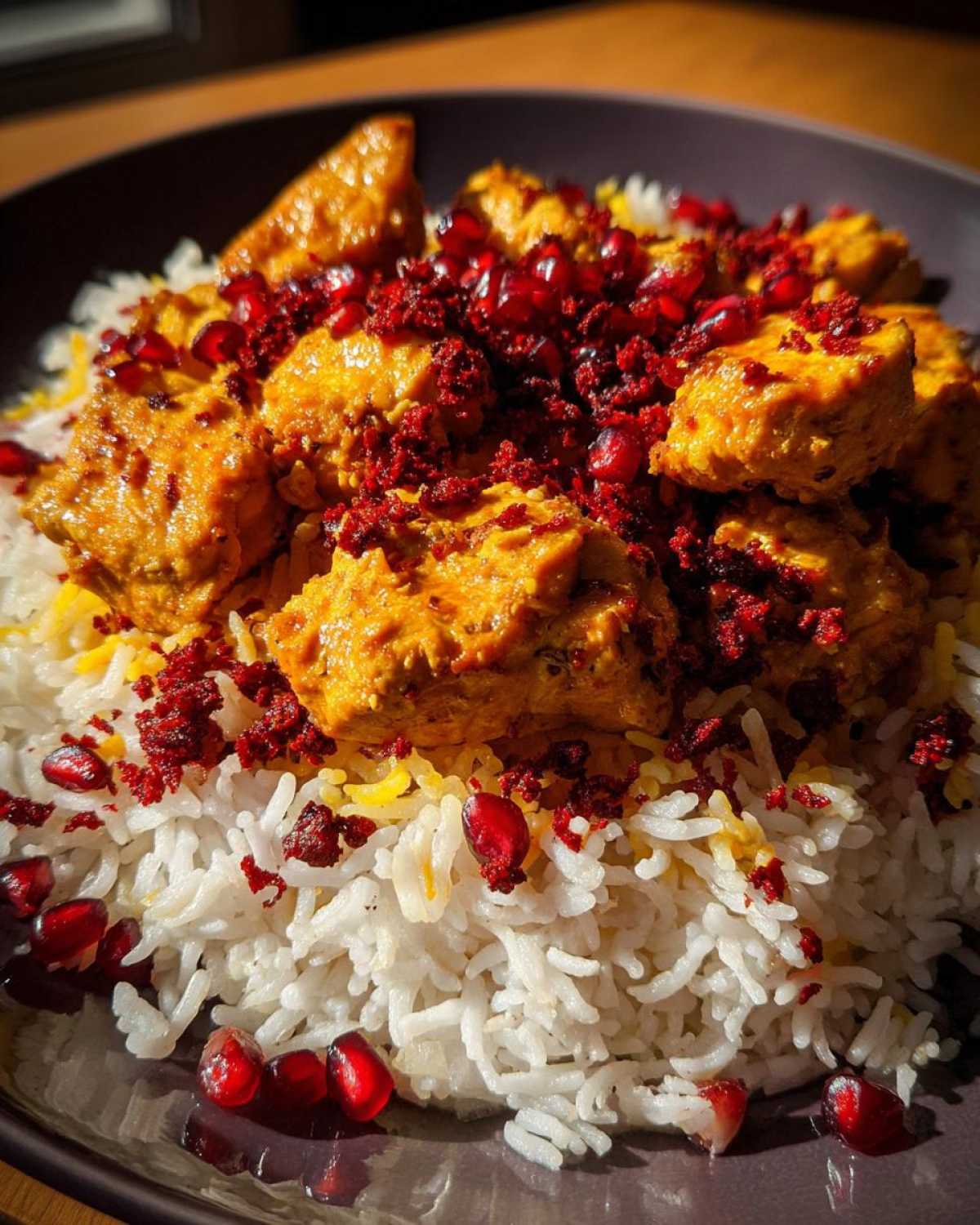 Close-up of vibrant Persian Chicken served over fluffy white rice, garnished heavily with bright red pomegranate seeds.