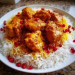 Close-up of succulent Persian Chicken pieces in a rich sauce served over fluffy white and saffron rice, garnished with bright pomegranate seeds.