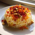 A molded serving of Persian Jeweled Rice Shirin Polo topped with pistachios, orange zest, and dried barberries.