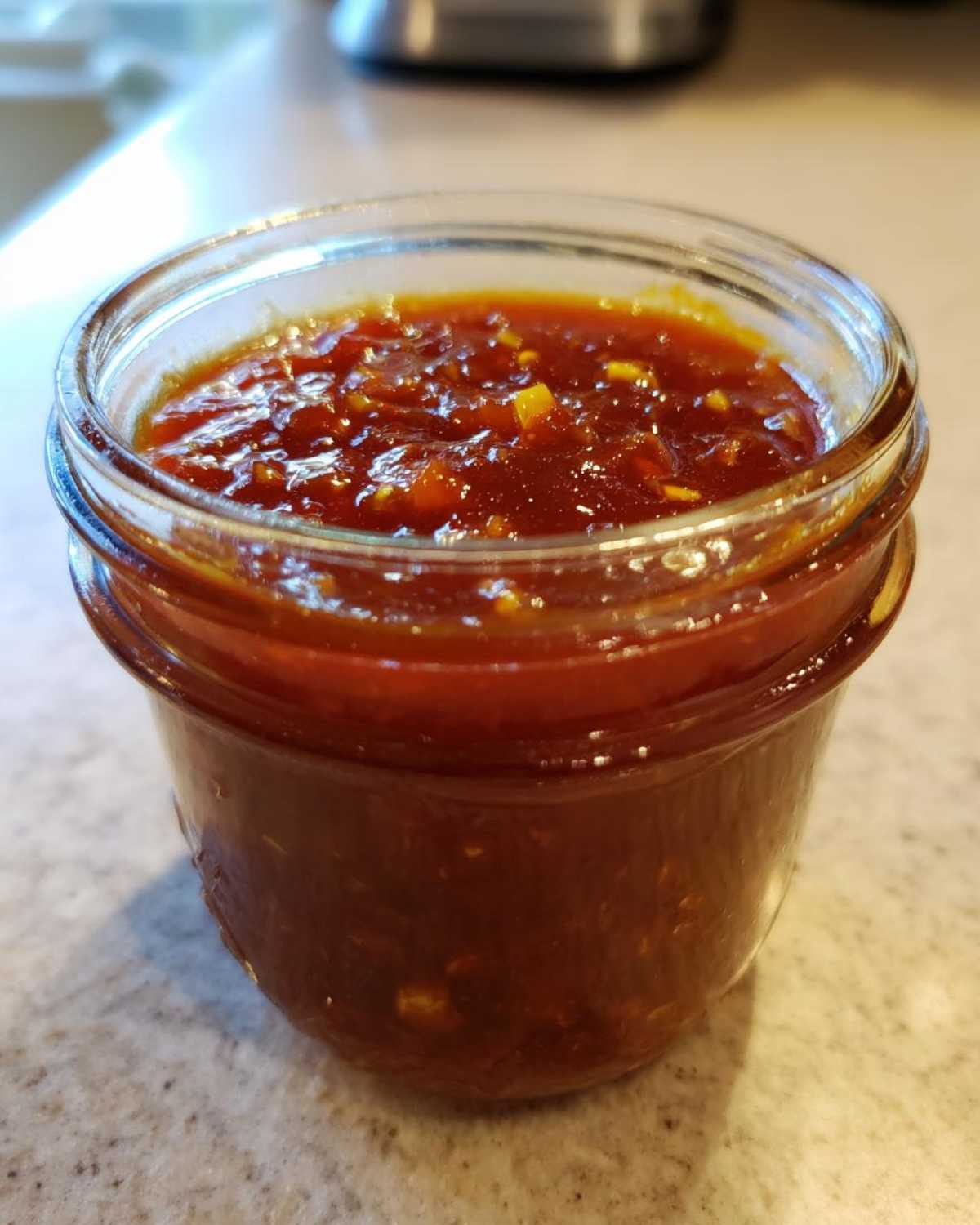 Close-up of a small glass jar filled with thick, chunky Pineapple Jalapeno Bourbon BBQ Sauce.