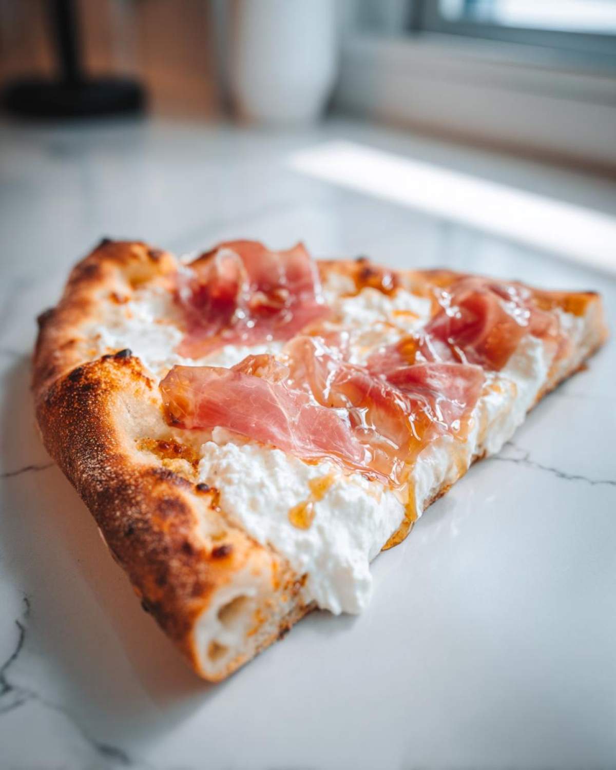 A close-up slice of Prosciutto Honey Burrata Pizza featuring creamy white cheese, draped prosciutto, and a drizzle of honey on a charred crust.