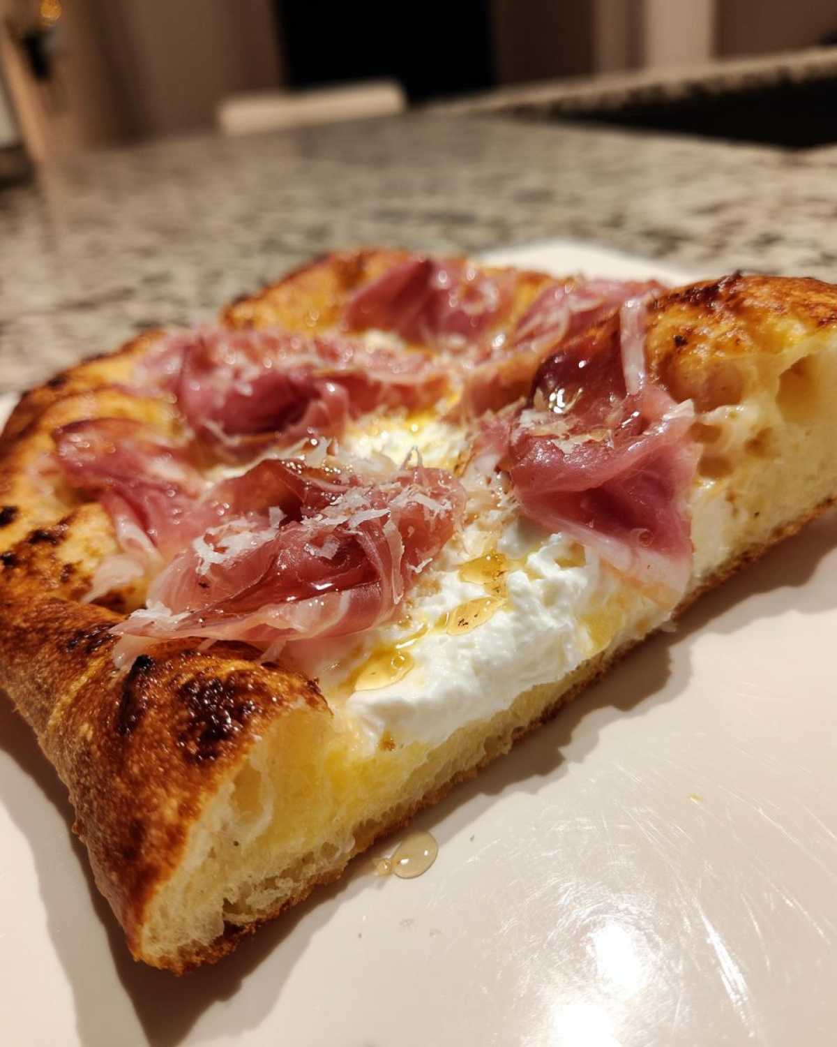 Close-up of a slice of Prosciutto Honey Burrata Pizza showing thick crust, white burrata, prosciutto, and drizzled honey.