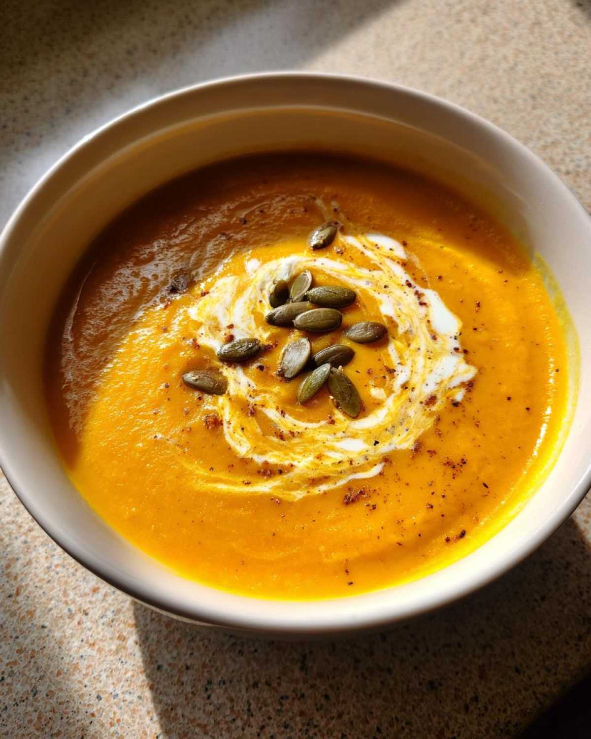 A close-up of vibrant orange Roasted Butternut Squash Soup topped with a swirl of cream and toasted pumpkin seeds.