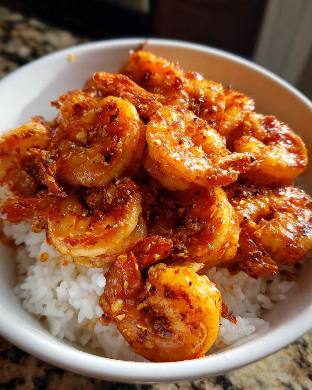 Close-up of a white bowl filled with white rice topped generously with bright orange Spicy Cajun Shrimp and Rice Bowl seasoning.