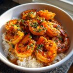 Close-up of a white bowl filled with white rice topped generously with glossy, orange-red Spicy Cajun Shrimp and fresh parsley.