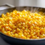 Close-up of bright yellow, steaming Buttered Corn kernels cooking in a dark skillet.