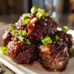 Close-up of glossy Sticky Hoisin Meatballs Asian Appetizer coated in sauce and topped with sesame seeds and green onions.