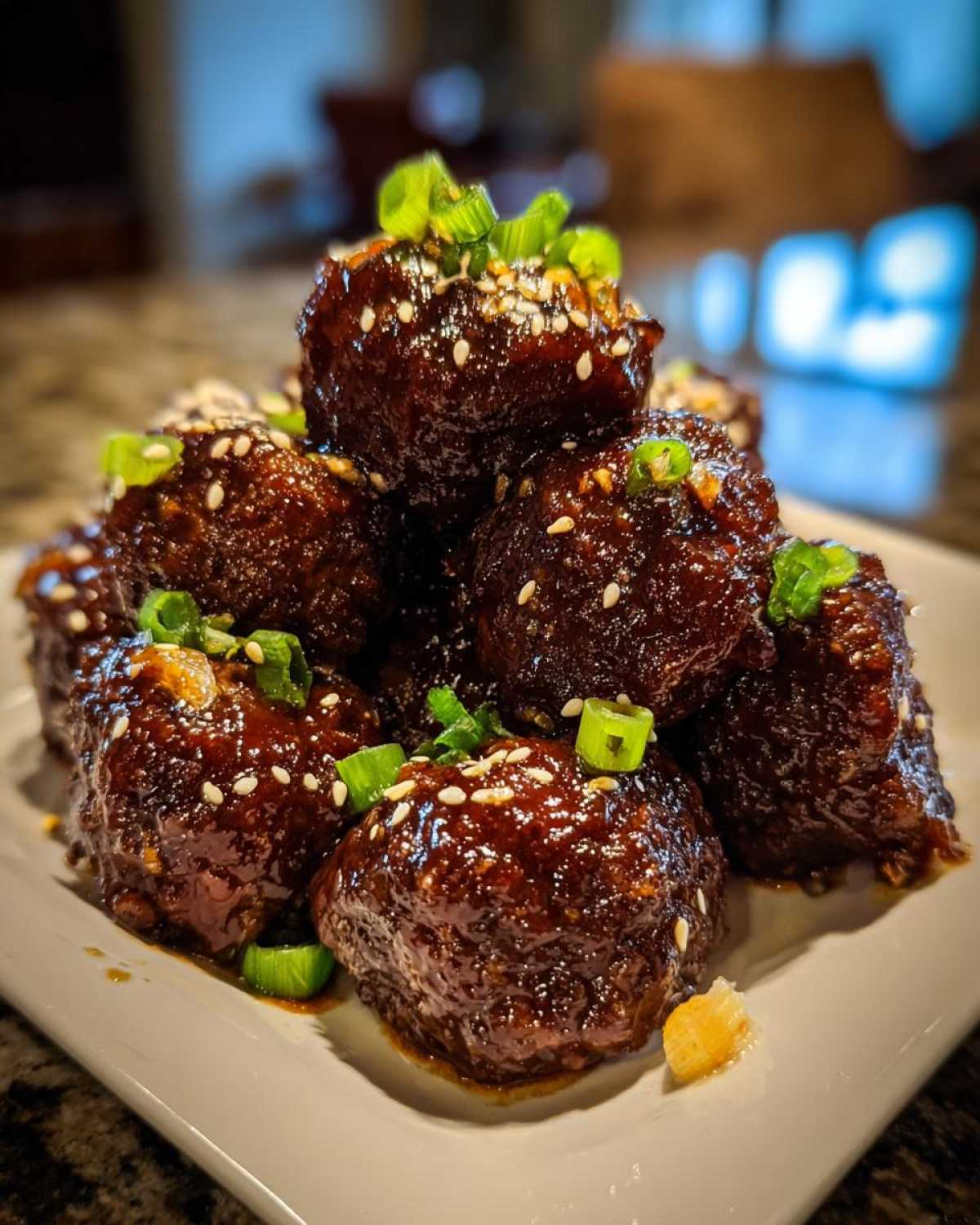 A close-up of several Sticky Hoisin Meatballs Asian Appetizer piled on a white plate, glazed and topped with sesame seeds and green onions.