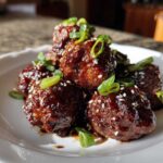 Close-up of several Sticky Hoisin Meatballs Asian Appetizer coated in a dark, glossy sauce, garnished with sesame seeds and sliced green onions.