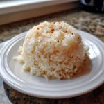 A perfectly molded serving of fluffy Texas Roadhouse Seasoned Rice topped with visible seasonings on a white plate.