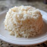 Molded serving of fluffy white Texas Roadhouse Seasoned Rice on a white plate.