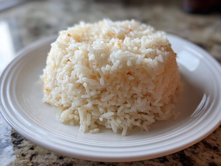 Molded serving of fluffy white Texas Roadhouse Seasoned Rice on a white plate.