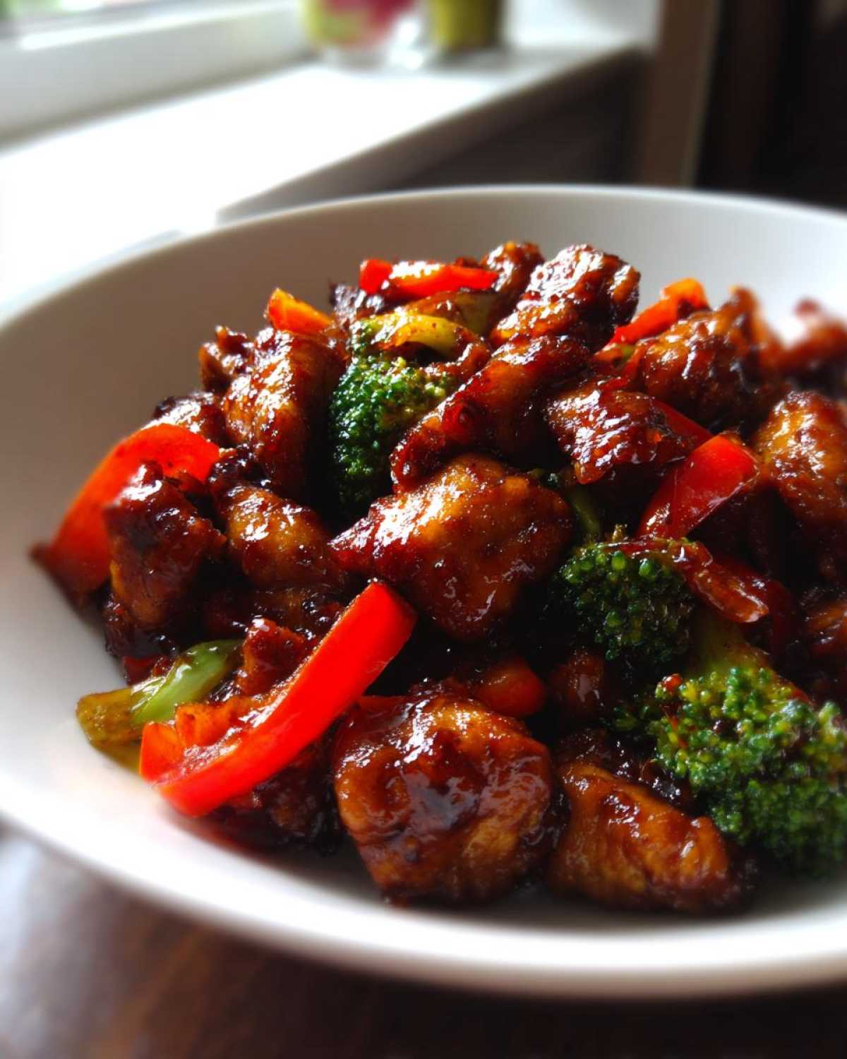 Close-up of glossy, saucy Thai Chicken Sweet and Spicy mixed with bright red peppers and green broccoli florets.