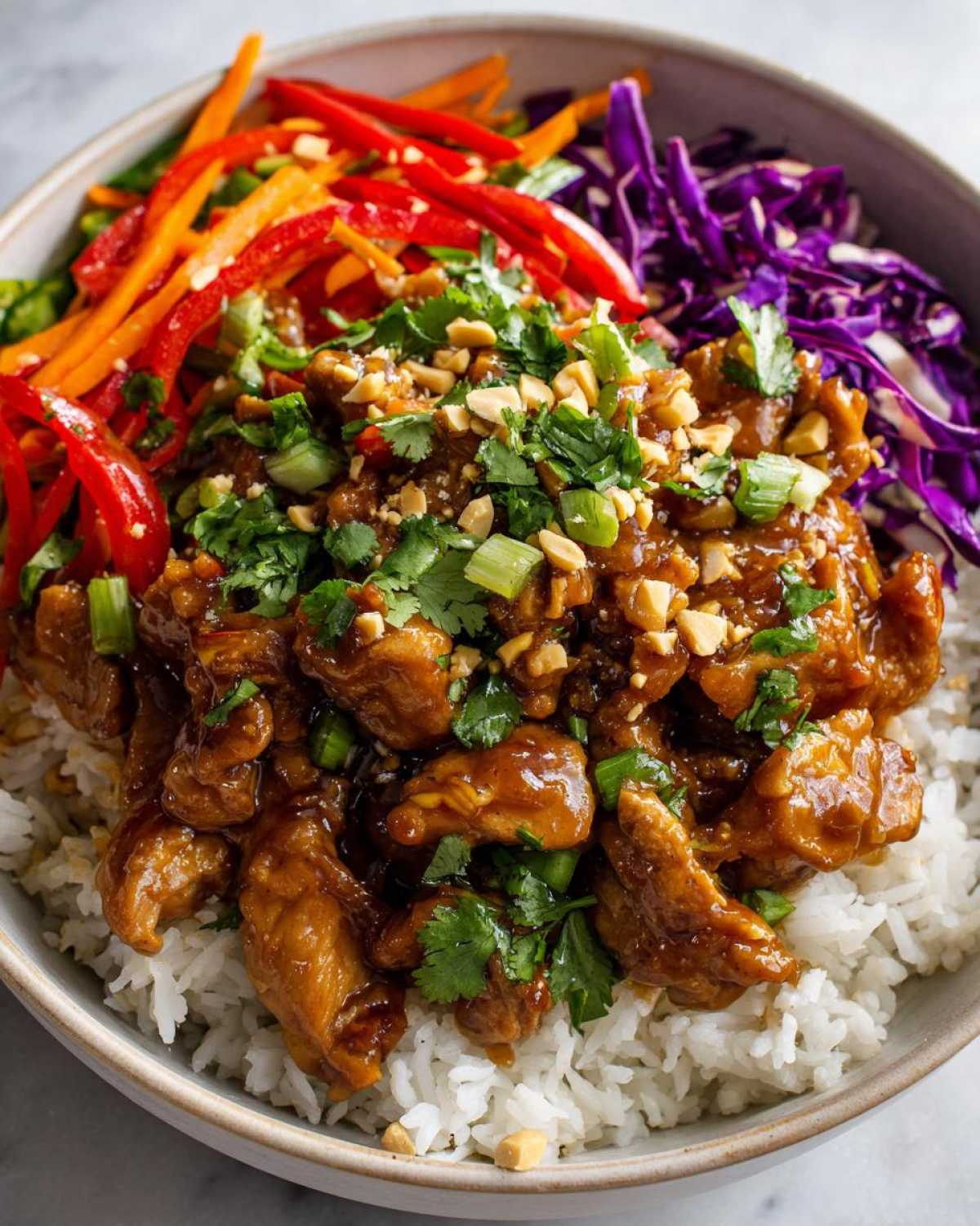 Close-up of a vibrant Thai Peanut Chicken Bowl featuring saucy chicken over white rice, topped with peanuts, cilantro, and shredded vegetables.