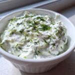 Close-up of thick, creamy Tzatziki Sauce garnished with fresh dill in a white bowl.