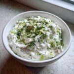 Close-up of thick, creamy Tzatziki Sauce topped with fresh dill and lime zest in a white bowl.