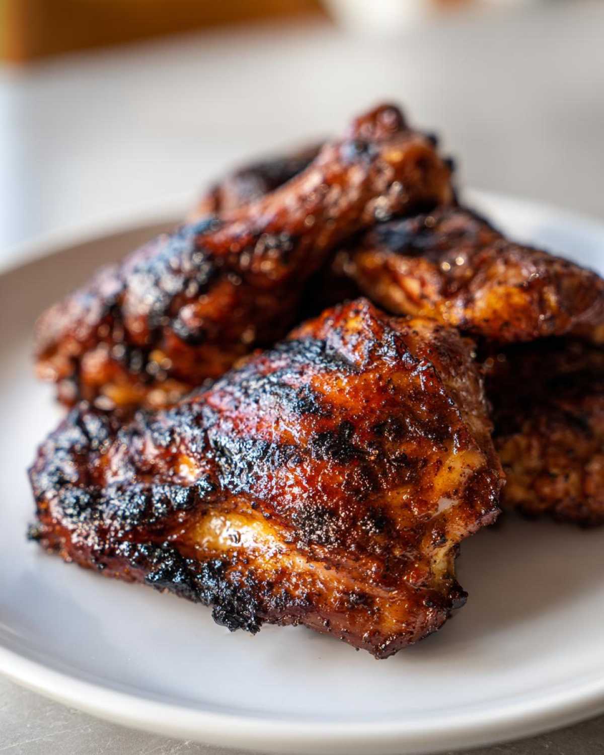 Close-up of several pieces of dark, caramelized Vietnamese Grilled Chicken with visible char marks, served on a white plate.