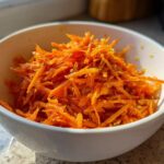 A close-up of bright orange shredded carrots in a white bowl, representing the Viral Tiktok Carrot Salad.