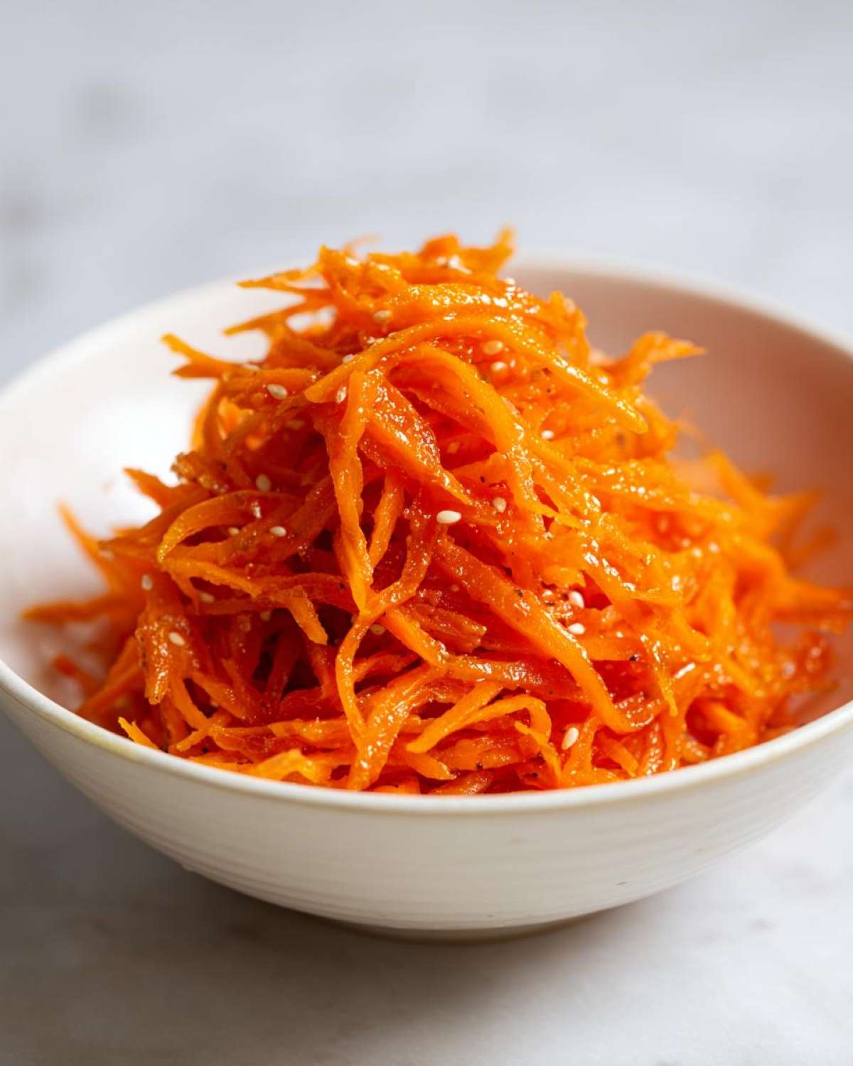 Close-up of bright orange, shredded carrots seasoned with sesame seeds, representing the Viral Tiktok Carrot Salad.