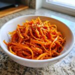 A white bowl filled with bright orange, julienned carrots seasoned and topped with sesame seeds, representing the Viral Tiktok Carrot Salad.
