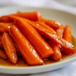Close-up of tender, bright orange Whiskey Glazed Carrots coated in a rich, amber glaze, served on a white dish.