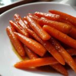 Close-up of vibrant, shiny Whiskey Glazed Carrots piled in a white serving bowl.