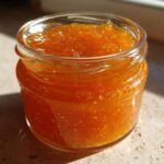 Close-up of a small glass jar filled with bright orange Apricot Jam with Vanilla Lemon.