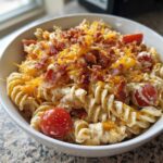A close-up of creamy Bacon Pasta Salad featuring rotini pasta, shredded cheddar cheese, bacon bits, and cherry tomatoes.
