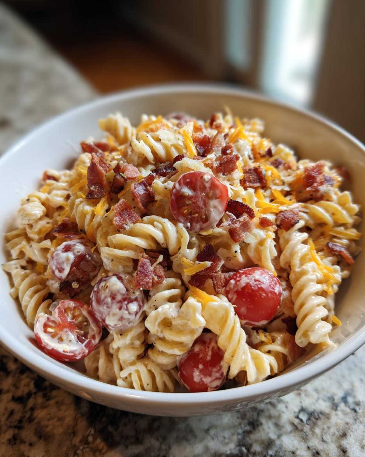 Close-up of a creamy Bacon Pasta Salad featuring rotini pasta, halved cherry tomatoes, bacon bits, and shredded cheese.