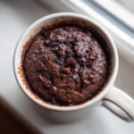 Close-up overhead view of a moist Dark Chocolate Banana Bread Mug Cake topped with melted chocolate chips in a white mug.