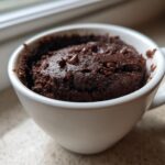 Close-up of a freshly baked Dark Chocolate Banana Bread Mug Cake topped with chocolate chips in a white mug.