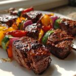 Close-up of glossy, glazed Steak Kebabs featuring chunks of seared beef interspersed with colorful bell peppers, zucchini, and red onion.