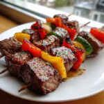 Close-up of perfectly grilled Steak Kebabs featuring juicy beef cubes, red and yellow bell peppers, and zucchini on a white plate.