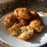 A plate of golden brown, crispy Crab Bombs, one broken open to show the shredded crab meat filling.