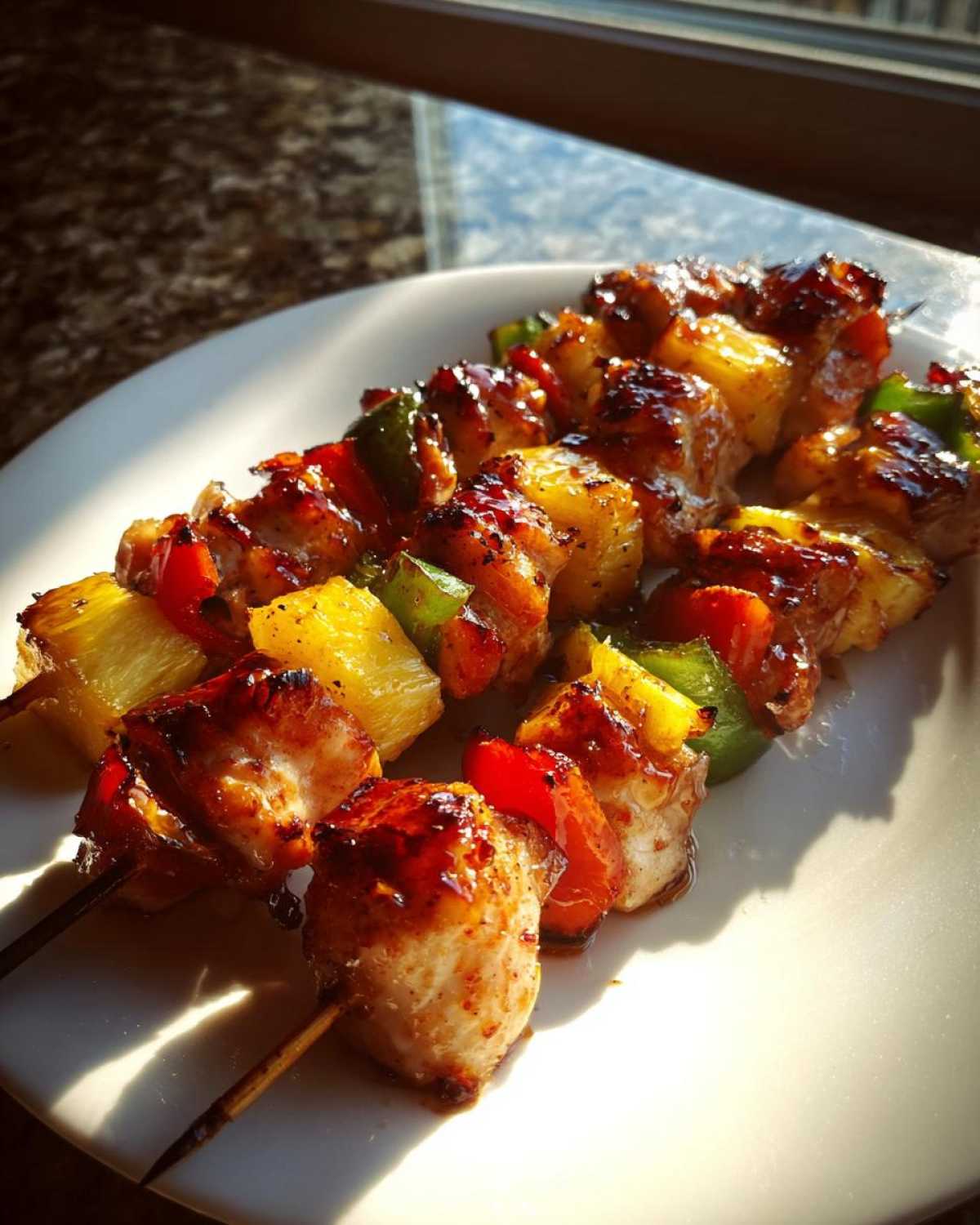 Close-up of three Grilled Pineapple Chicken Kabobs glistening with teriyaki glaze on a white plate.