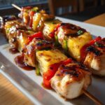 Close-up of several Grilled Pineapple Chicken Kabobs glistening with teriyaki glaze on a white platter.