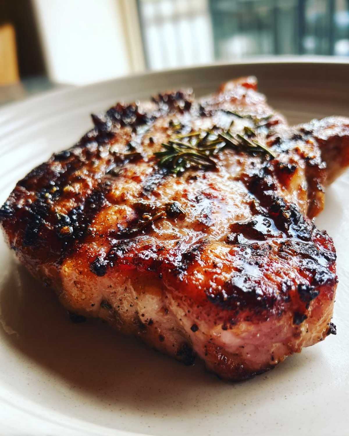 Close-up of a juicy, caramelized Grilled Rosemary Pork Chop garnished with a sprig of rosemary.