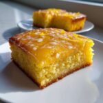 A close-up of a moist, square Lemon Brownies slice topped with bright yellow glaze and zest.