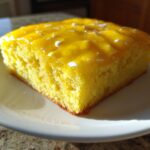 A square slice of bright yellow Lemon Brownies topped with a shiny lemon glaze and white sprinkles.