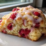 A close-up of a single, freshly baked Lemon Raspberry Scones slice topped with a sweet white glaze.