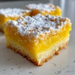 A close-up, tempting shot of a square Mango Lemon Bars slice topped generously with white powdered sugar.