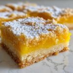 A close-up of a square Mango Lemon Bars slice showing the bright yellow filling, shortbread crust, and a dusting of powdered sugar.