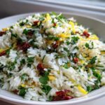 A white bowl filled with fluffy Mediterranean Rice mixed with chopped parsley, sun-dried tomatoes, and bright lemon zest.