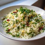 A white bowl filled with bright Mediterranean Rice, topped generously with fresh parsley, lemon zest, and sun-dried tomatoes.