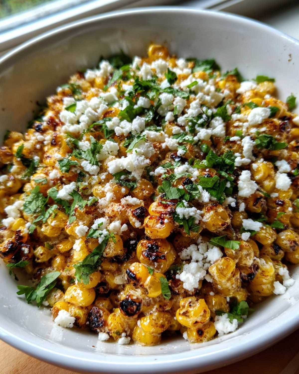 Close-up of roasted corn kernels topped with crumbled white cheese and cilantro, ready to serve as Mexican Street Corn Salad.