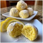 A close-up of a No Bake Lemon Truffles cut in half, showing the texture, dusted with powdered sugar, next to lemon slices.