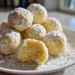 A stack of bright yellow No Bake Lemon Truffles generously coated in white powdered sugar on a white plate.