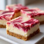A square piece of No Bake Rhubarb Bars showing a thick graham cracker crust and a creamy cheesecake layer swirled with bright red rhubarb puree.